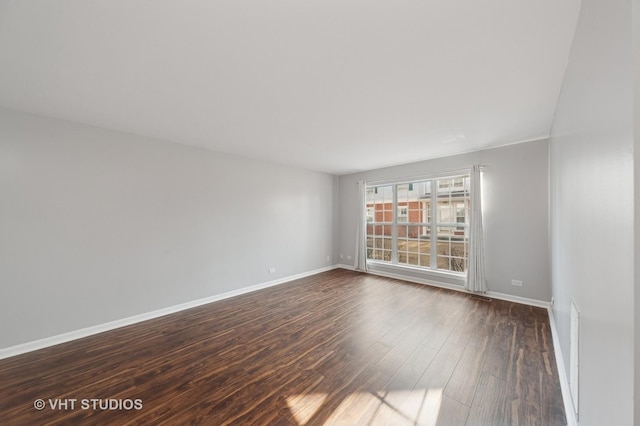 spare room with baseboards and dark wood-type flooring