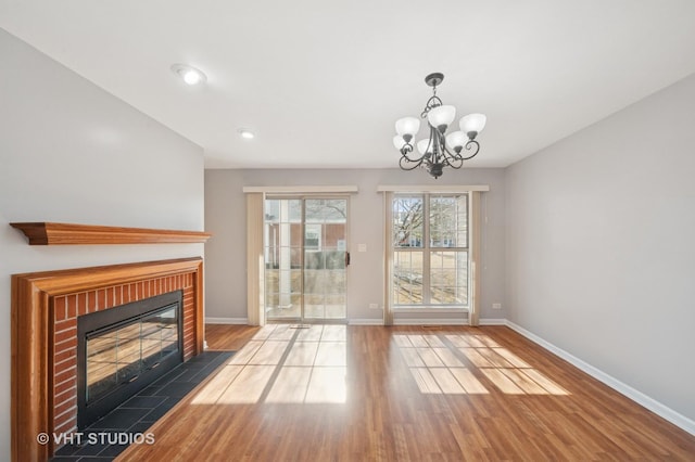 unfurnished living room with an inviting chandelier, a brick fireplace, baseboards, and wood finished floors