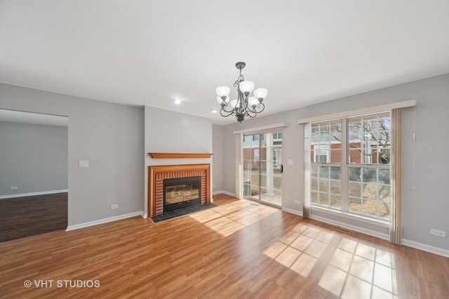 unfurnished living room featuring visible vents, baseboards, a fireplace, an inviting chandelier, and wood finished floors