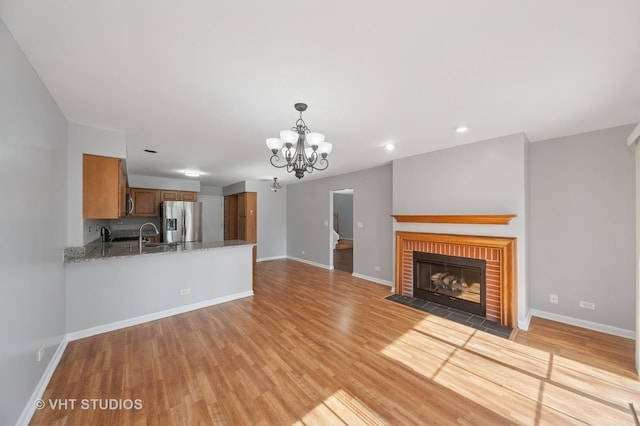 unfurnished living room with a chandelier, light wood-style flooring, a fireplace, and baseboards