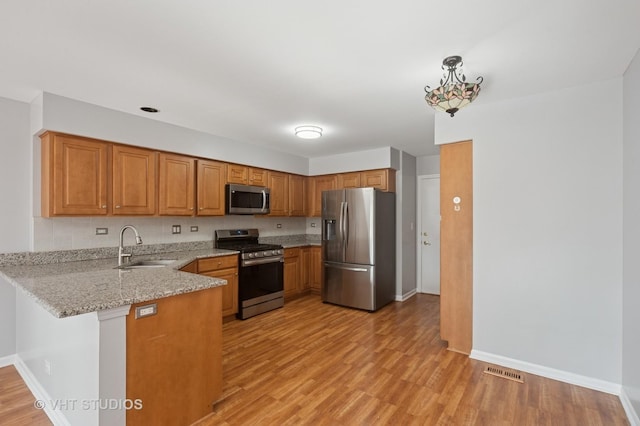 kitchen with brown cabinets, a sink, stainless steel appliances, light wood-style floors, and a peninsula