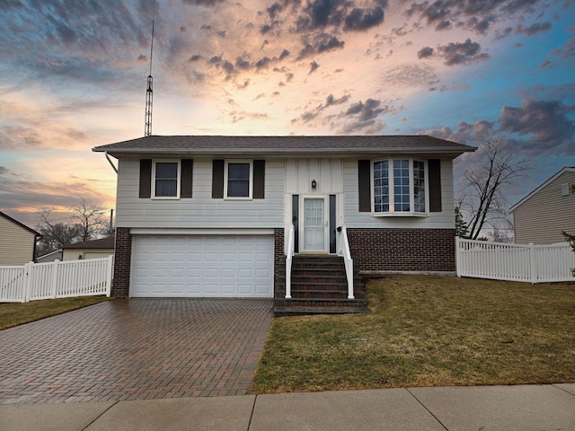 raised ranch featuring decorative driveway, brick siding, and fence