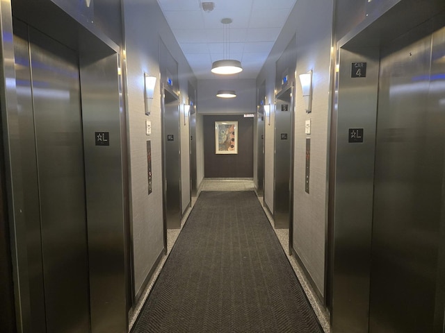 corridor featuring dark colored carpet, elevator, and a package area