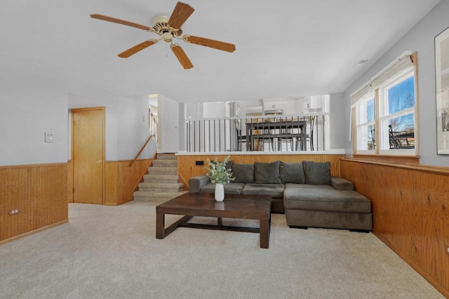 living area with ceiling fan, carpet floors, wood walls, stairway, and wainscoting