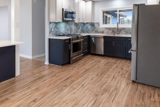 kitchen with a sink, white cabinetry, light wood-style floors, light countertops, and appliances with stainless steel finishes