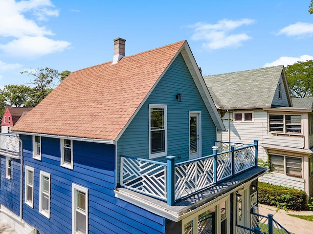 back of house featuring a balcony, a shingled roof, and a chimney