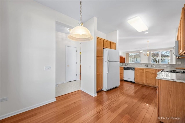 kitchen with pendant lighting, white appliances, a sink, and light wood finished floors