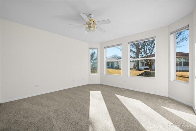 carpeted spare room featuring plenty of natural light, baseboards, and ceiling fan