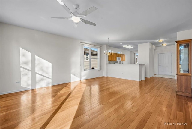 unfurnished living room featuring light wood finished floors and ceiling fan with notable chandelier