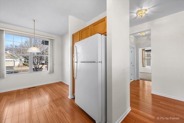 kitchen with baseboards, brown cabinets, wood finished floors, freestanding refrigerator, and hanging light fixtures