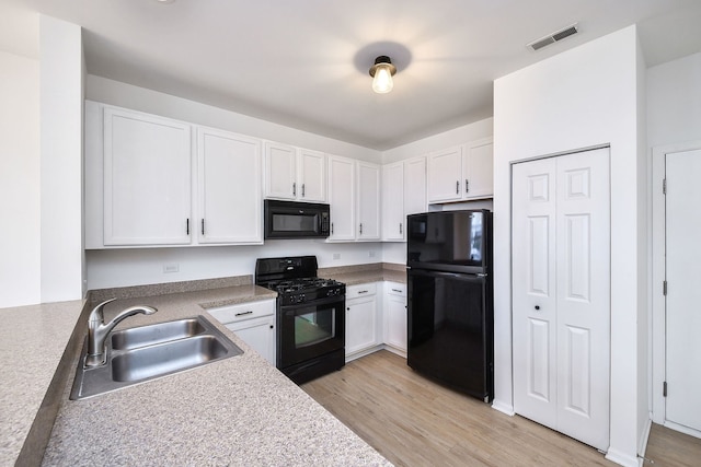 kitchen with black appliances, light wood finished floors, a sink, and white cabinets