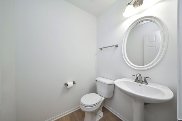 half bath with baseboards, toilet, and wood finished floors