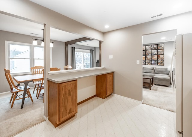 kitchen with light countertops, visible vents, brown cabinetry, freestanding refrigerator, and baseboards