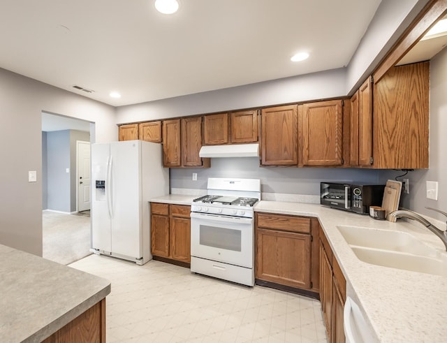 kitchen featuring light floors, brown cabinetry, a sink, white appliances, and under cabinet range hood