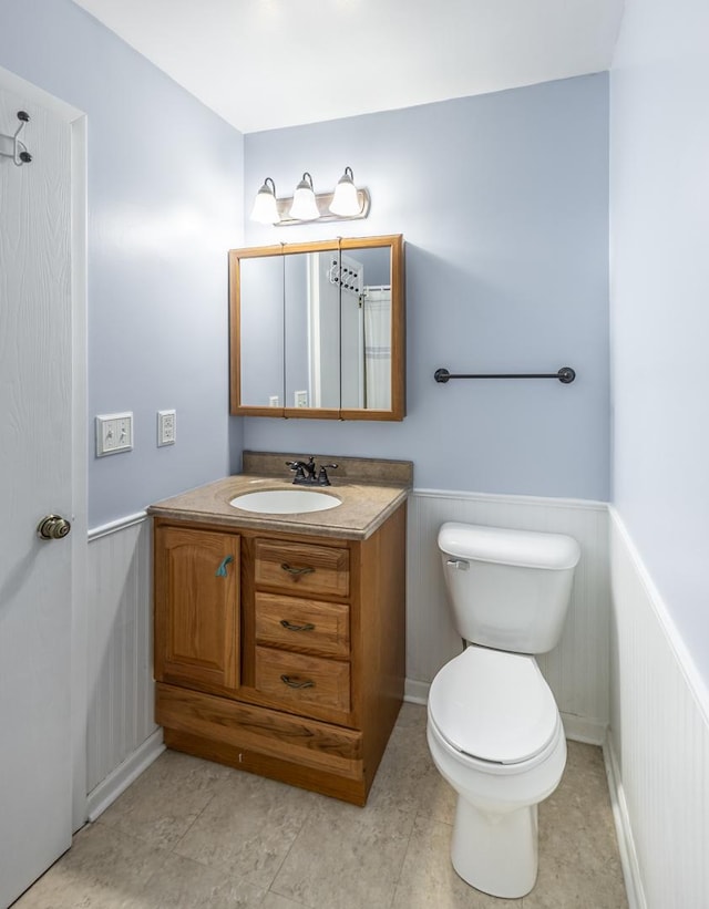 bathroom with a wainscoted wall, toilet, vanity, and tile patterned floors