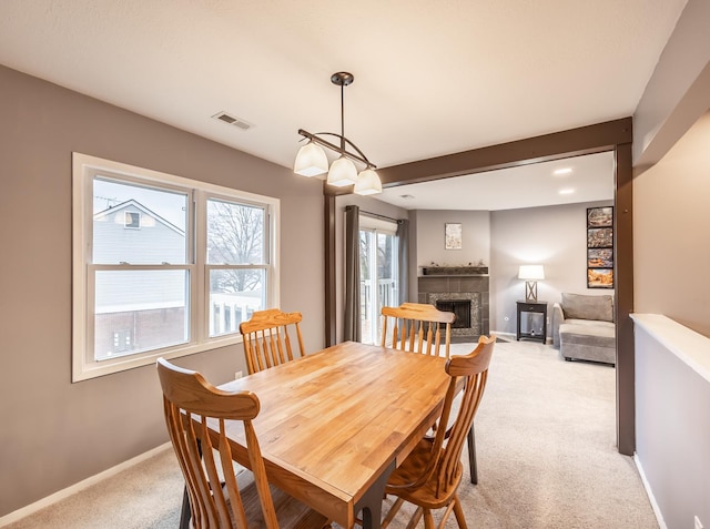 dining room featuring light carpet, baseboards, visible vents, a tile fireplace, and beamed ceiling