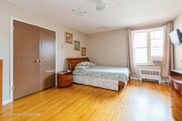 bedroom featuring radiator, baseboards, light wood-type flooring, and a closet