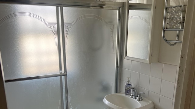 bathroom with plenty of natural light, a shower with shower door, a sink, and tile walls