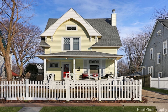 view of front of property featuring a chimney, a porch, a fenced front yard, and a shingled roof