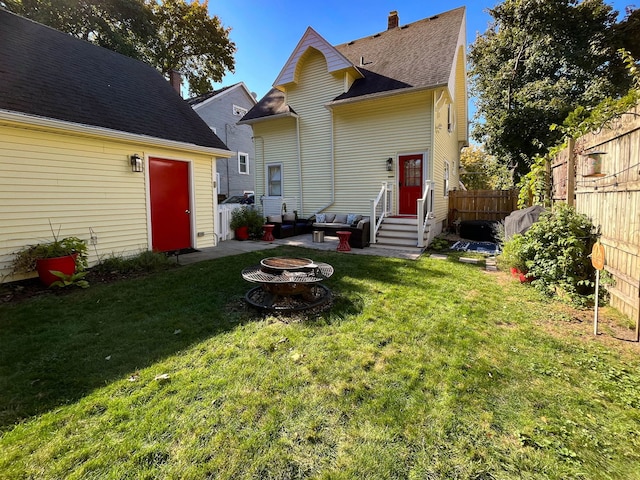 rear view of house with entry steps, a yard, an outdoor fire pit, and fence