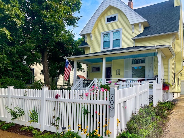 view of front of house with a fenced front yard, covered porch, roof with shingles, and a chimney