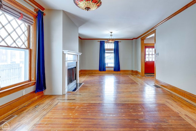 unfurnished living room featuring wood finished floors, ornamental molding, a fireplace with flush hearth, and visible vents