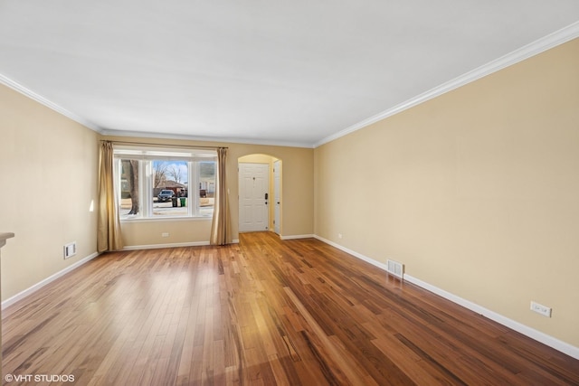 spare room featuring baseboards, visible vents, arched walkways, wood finished floors, and crown molding