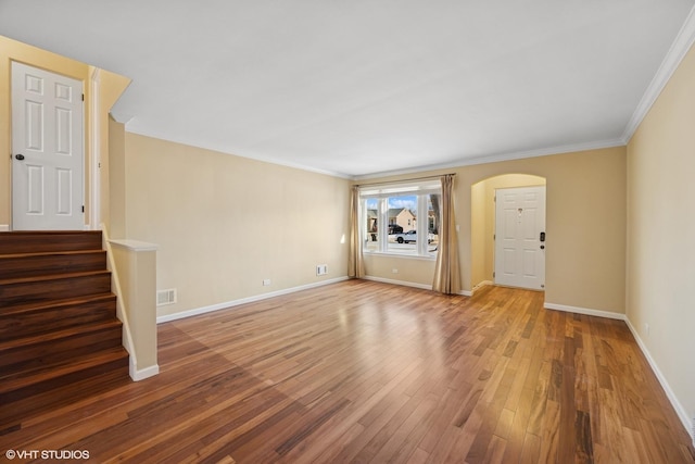 spare room featuring arched walkways, wood finished floors, visible vents, baseboards, and stairway