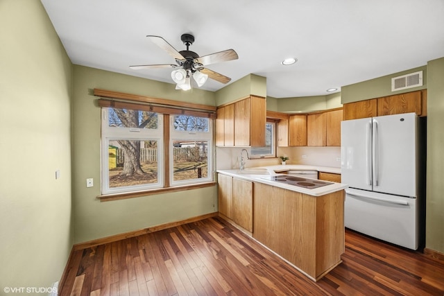 kitchen with visible vents, freestanding refrigerator, a peninsula, light countertops, and a sink