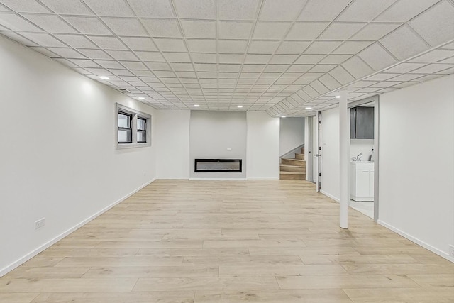 finished basement with baseboards, light wood-style floors, a glass covered fireplace, and stairs