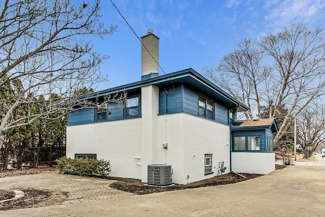 view of side of property featuring brick siding, central AC, and a chimney