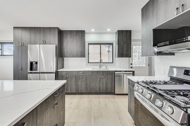 kitchen featuring a wealth of natural light, light stone counters, appliances with stainless steel finishes, and a sink