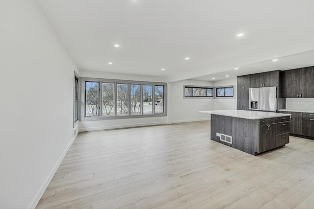 kitchen with a kitchen island, light countertops, light wood-style flooring, recessed lighting, and stainless steel fridge