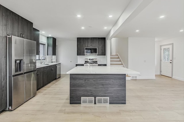 kitchen featuring visible vents, a kitchen island, light wood-style flooring, a sink, and stainless steel appliances