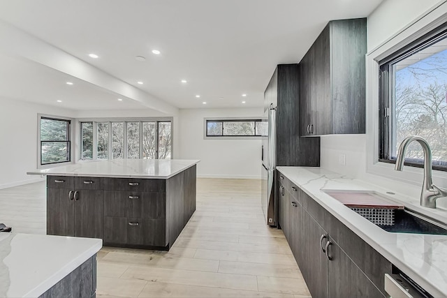 kitchen featuring modern cabinets, a sink, light stone counters, a kitchen island, and recessed lighting