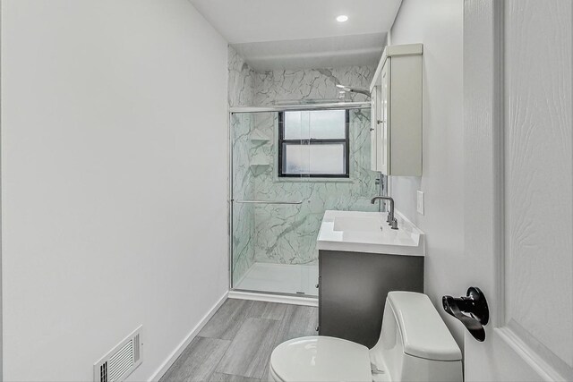 bathroom featuring a marble finish shower, visible vents, toilet, wood finished floors, and vanity