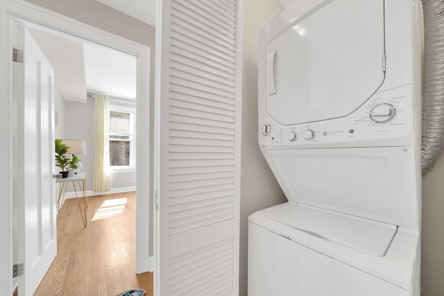 laundry room featuring laundry area, light wood-style flooring, stacked washing maching and dryer, and baseboards