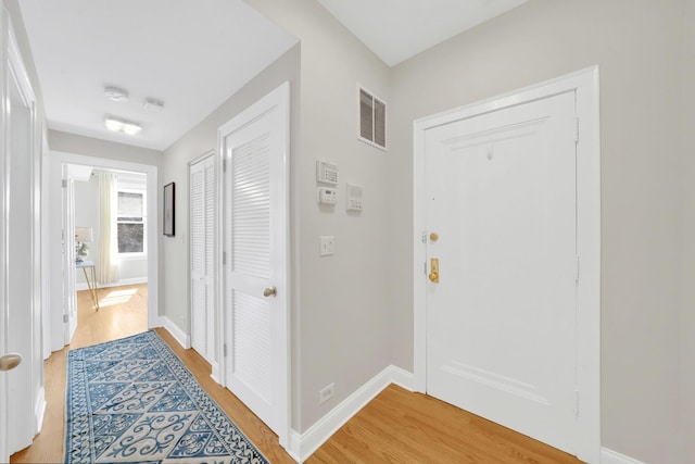 hallway featuring baseboards, visible vents, and light wood finished floors