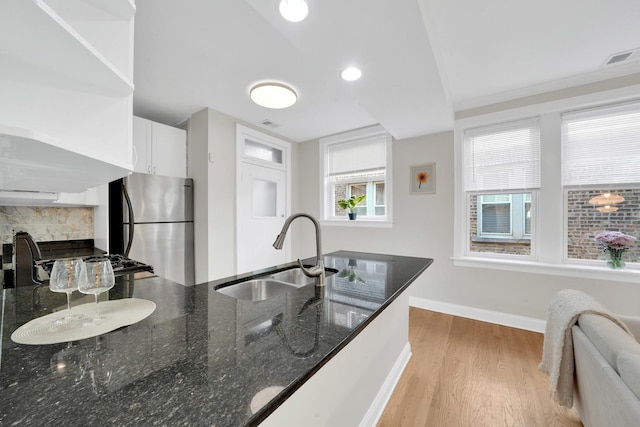 kitchen featuring a sink, dark stone countertops, freestanding refrigerator, light wood-style floors, and baseboards