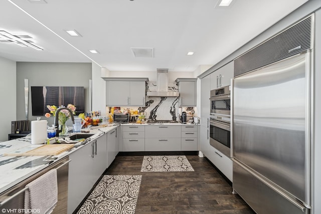 kitchen featuring a sink, range hood, appliances with stainless steel finishes, gray cabinets, and dark wood-style flooring