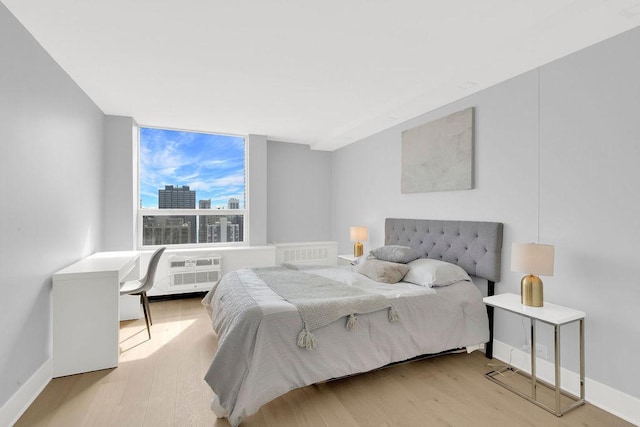bedroom with a wall of windows, baseboards, a view of city, and wood finished floors