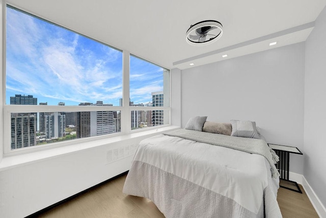 bedroom featuring a view of city, wood finished floors, baseboards, and recessed lighting