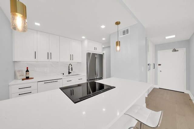 kitchen featuring a sink, visible vents, stainless steel refrigerator, black electric stovetop, and white dishwasher