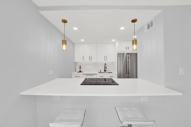 kitchen with freestanding refrigerator, visible vents, a sink, white cabinetry, and stovetop