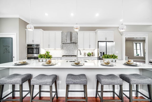 kitchen featuring a large island, ornamental molding, a sink, stainless steel appliances, and wall chimney exhaust hood