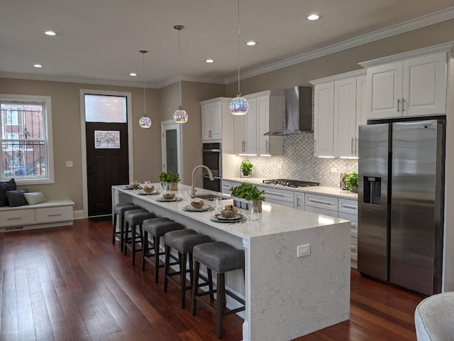 kitchen with a kitchen island with sink, a sink, stainless steel appliances, wall chimney exhaust hood, and white cabinets