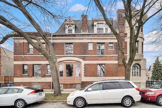 view of front facade featuring fence, brick siding, roof with shingles, and a chimney