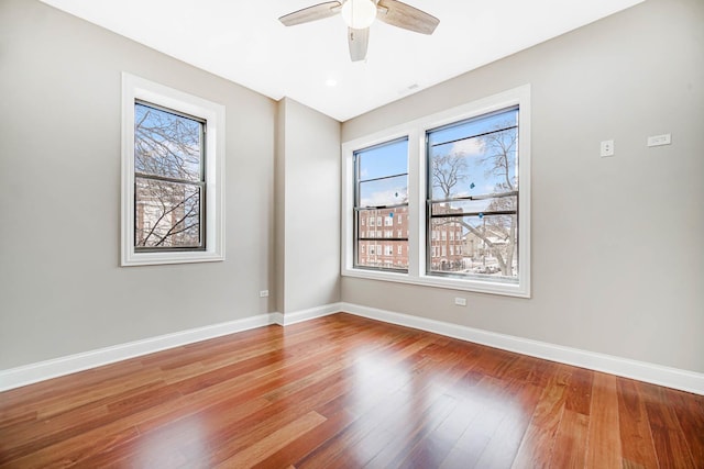 spare room with wood finished floors, a healthy amount of sunlight, baseboards, and ceiling fan