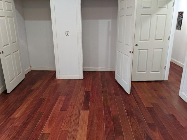 unfurnished bedroom with a closet, baseboards, and dark wood-type flooring