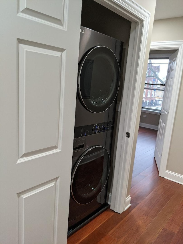 washroom with baseboards, wood finished floors, laundry area, and stacked washing maching and dryer